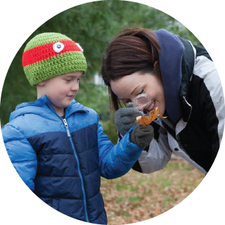 Kid in jacket with mom looking through magnifying glass