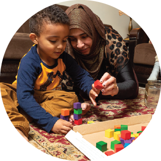 A mother and child examine a red building block.
