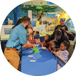 An adult hands out materials to several children at a science event