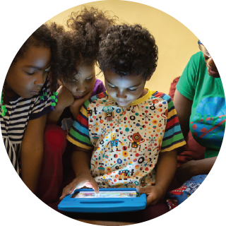 A boy interacts with a tablet as two girls and an adult stand by him
