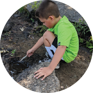 A boy uses a stick to explore a small puddle