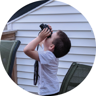 A boy uses binoculars to look up at the sky