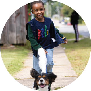 A boy smiles as he walks the dog.