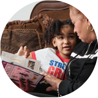 A boy looks up at an adult as they read a book.