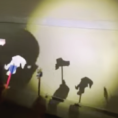 A family making shadow puppets with heavy paper, tape, and tongue depressors