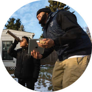 Kid looking through a telescope with Dad holding an iPad